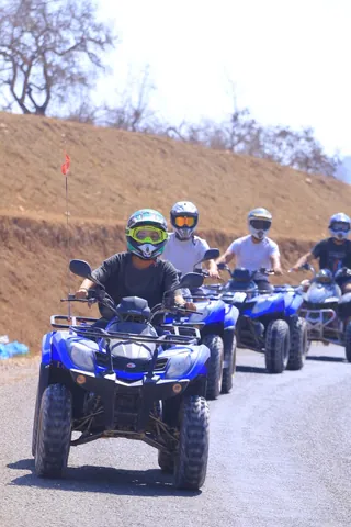Helmeted guests riding blue quads along a mountain road