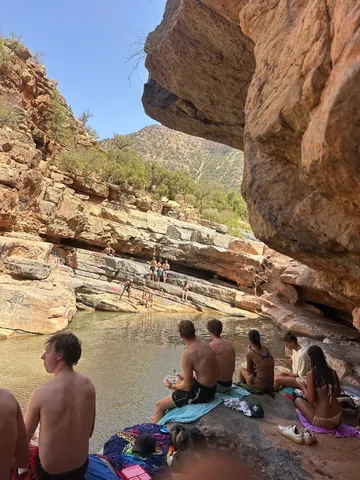 Visitors resting beside a natural pool under a rocky overhang