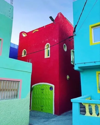 Pink and turquoise buildings with a green door in Aghroud