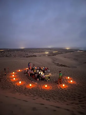 A gathering on the dunes surrounded by evening lights