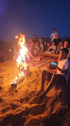 Guests sitting beside a fire on the sand in the evening