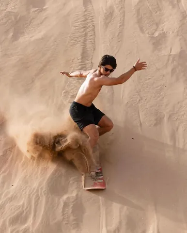 A rider sandboarding down a steep sand dune